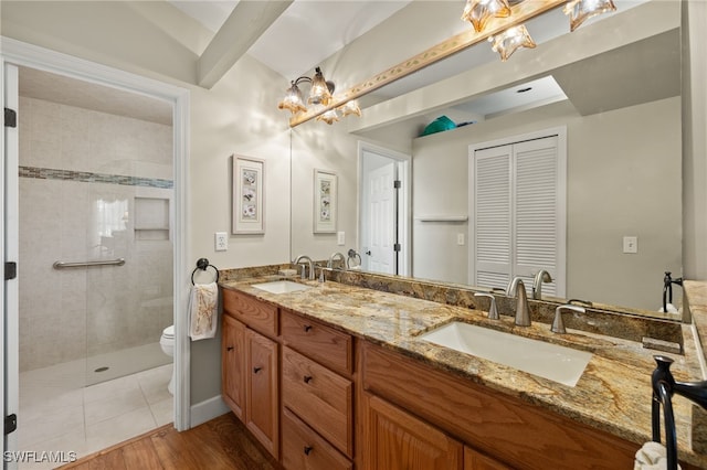 bathroom with double vanity, toilet, tiled shower, and a sink