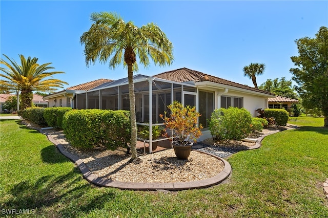 rear view of house featuring glass enclosure, a tiled roof, a yard, and stucco siding