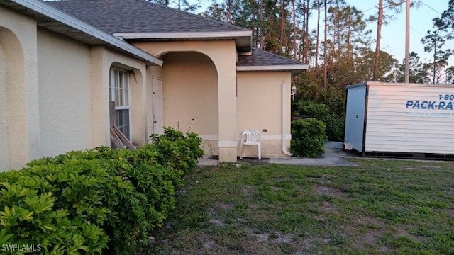 property entrance with stucco siding, a yard, and a shingled roof