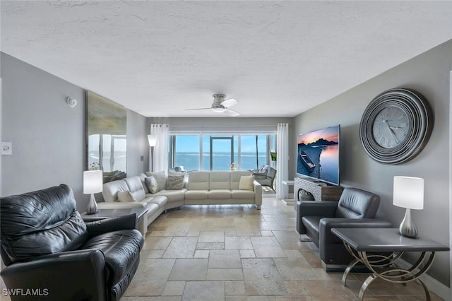 living room with stone tile floors, a ceiling fan, baseboards, and a textured ceiling