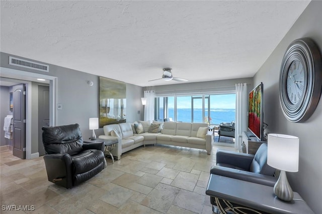 living room featuring visible vents, baseboards, ceiling fan, stone tile flooring, and a textured ceiling