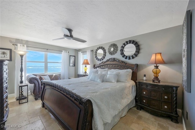 bedroom featuring a textured ceiling, a ceiling fan, baseboards, and stone tile flooring