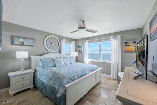 bedroom with ceiling fan, baseboards, a textured ceiling, and stone tile flooring