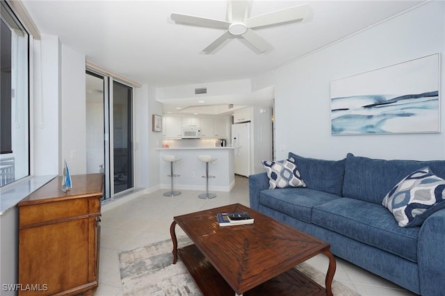 living area featuring light tile patterned flooring, a ceiling fan, visible vents, and baseboards