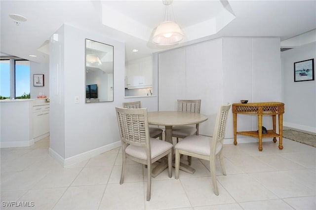 dining space with a tray ceiling, baseboards, and light tile patterned flooring