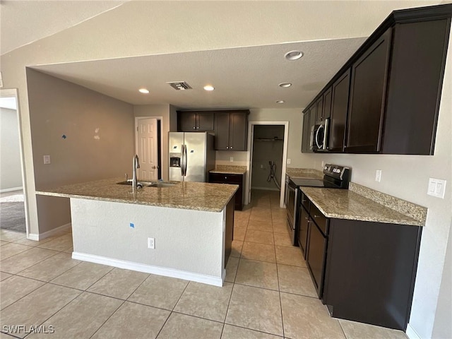 kitchen featuring an island with sink, a sink, light stone counters, stainless steel appliances, and light tile patterned flooring