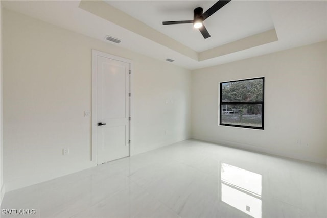 empty room featuring a raised ceiling, a ceiling fan, and visible vents