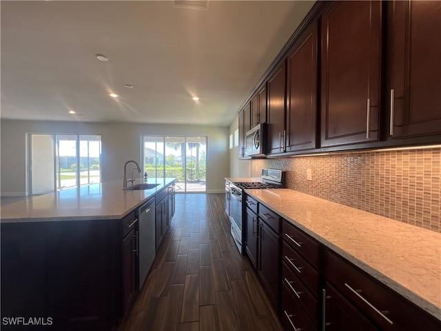 kitchen with a sink, backsplash, dark wood finished floors, stainless steel appliances, and a kitchen island with sink