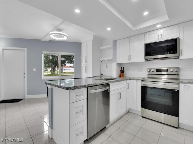 kitchen with tasteful backsplash, appliances with stainless steel finishes, a peninsula, white cabinetry, and a sink