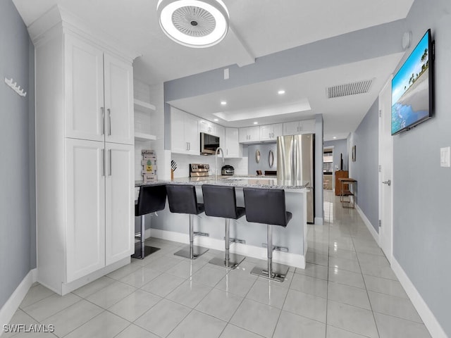 kitchen featuring visible vents, light stone counters, a tray ceiling, white cabinetry, and a peninsula