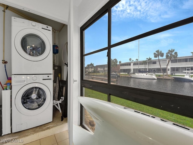 clothes washing area featuring tile patterned flooring, laundry area, a water view, and stacked washer and dryer