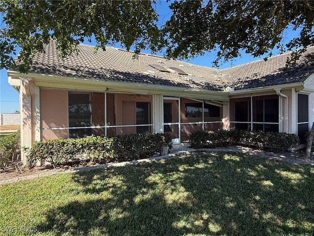 rear view of house featuring a lawn, a tiled roof, and a sunroom