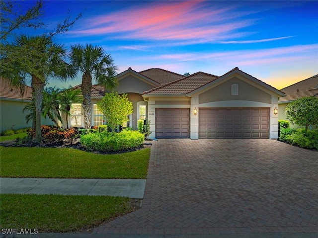 view of front of home with stucco siding, decorative driveway, a yard, a garage, and a tiled roof