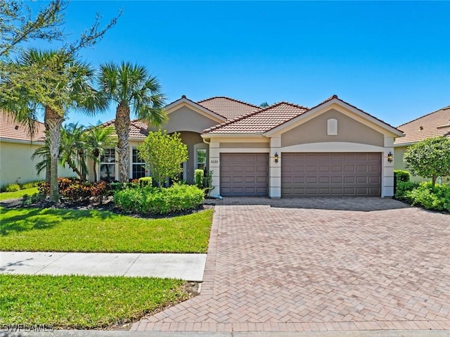 view of front facade with a tiled roof, a front yard, stucco siding, decorative driveway, and an attached garage