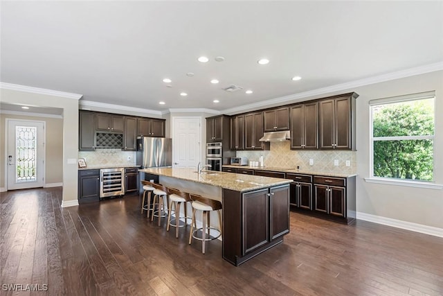 kitchen with under cabinet range hood, dark wood-type flooring, dark brown cabinets, and beverage cooler