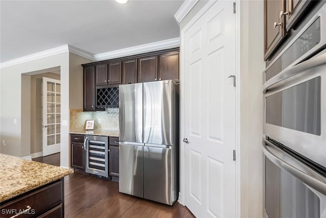 kitchen with beverage cooler, dark wood finished floors, ornamental molding, dark brown cabinets, and appliances with stainless steel finishes