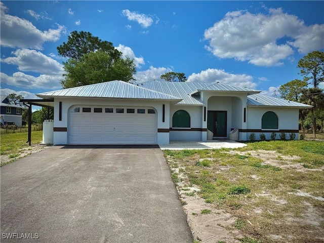 view of front of property with stucco siding, an attached garage, driveway, and metal roof