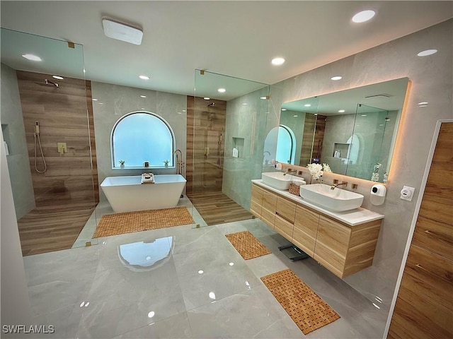 full bath featuring a freestanding bath, tile walls, a walk in shower, and a sink