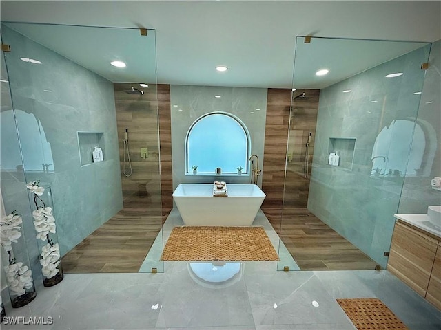 full bath with a freestanding tub, tiled shower, tile walls, and vanity