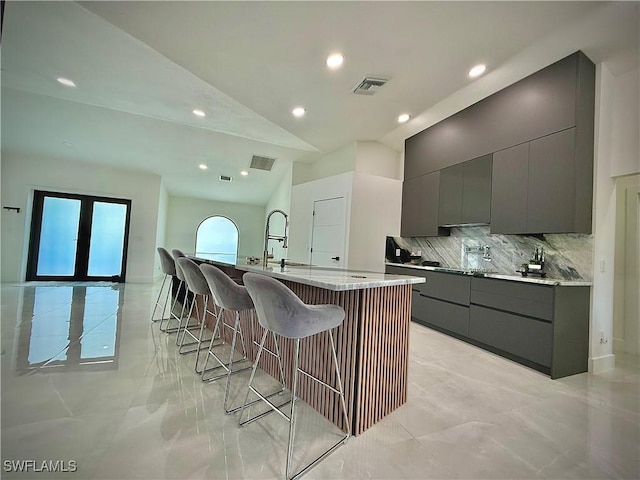 kitchen featuring visible vents, a kitchen bar, gray cabinets, a large island with sink, and a sink