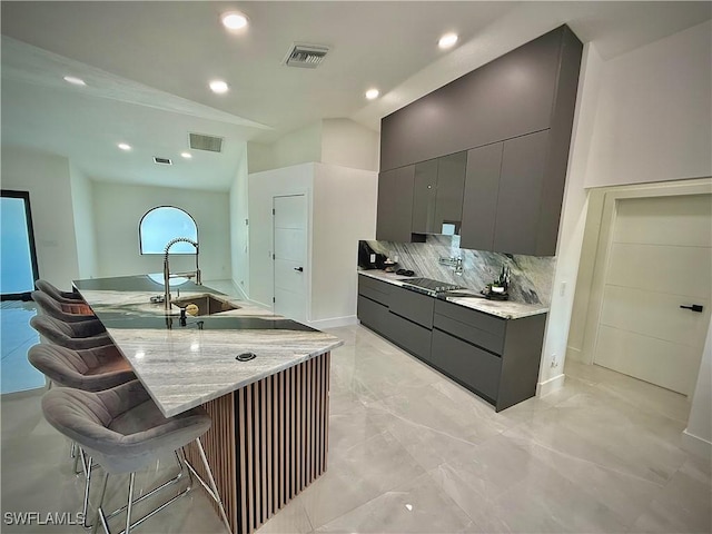 kitchen with visible vents, a breakfast bar, decorative backsplash, gray cabinets, and a sink