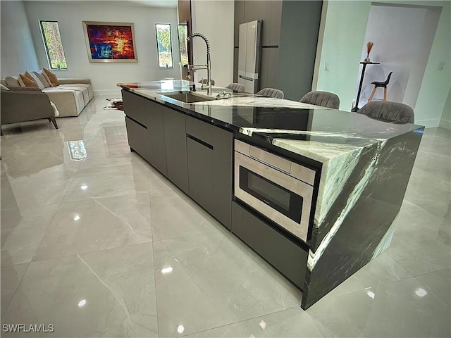 kitchen with marble finish floor, modern cabinets, a sink, stainless steel microwave, and a large island with sink