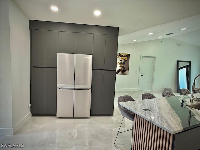 kitchen featuring light stone counters, freestanding refrigerator, gray cabinetry, a kitchen breakfast bar, and modern cabinets