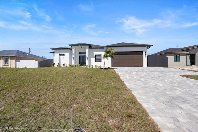 prairie-style home featuring a garage, decorative driveway, a front yard, and fence