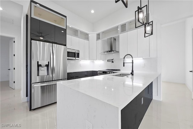 kitchen featuring a sink, light stone counters, stainless steel appliances, a peninsula, and wall chimney range hood