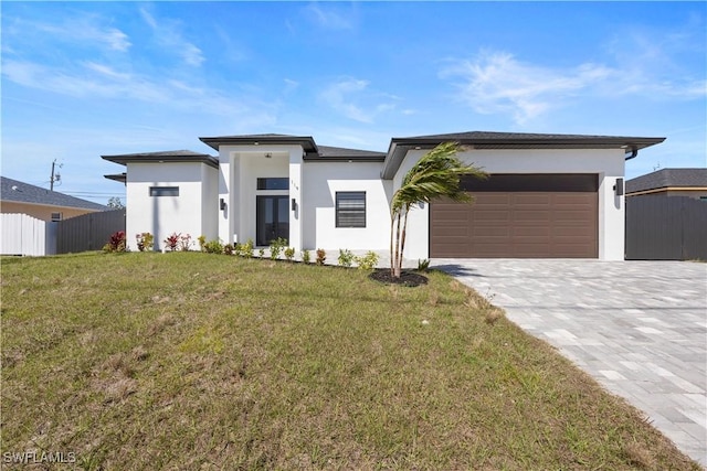 prairie-style house with a front yard, fence, an attached garage, stucco siding, and decorative driveway