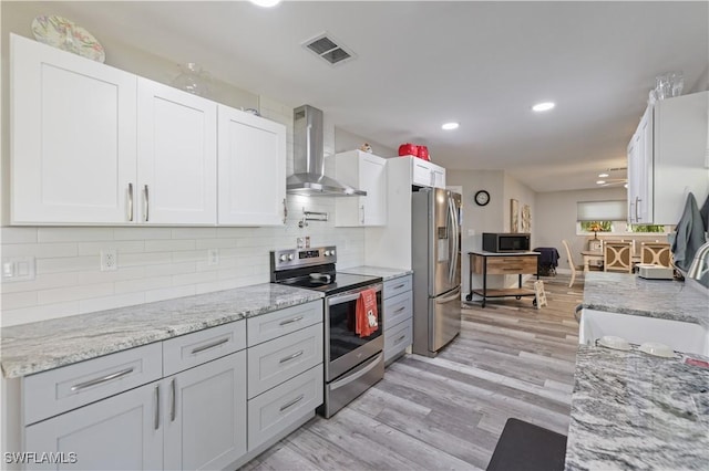 kitchen featuring tasteful backsplash, visible vents, light wood-style floors, stainless steel appliances, and wall chimney exhaust hood