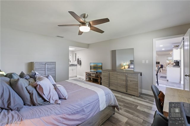 bedroom featuring a ceiling fan, baseboards, visible vents, ensuite bath, and light wood-type flooring