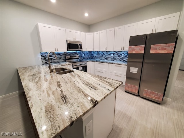 kitchen featuring light stone counters, decorative backsplash, a peninsula, stainless steel appliances, and a sink