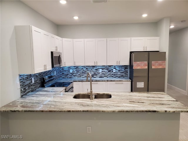 kitchen featuring a sink, backsplash, stainless steel appliances, a peninsula, and light stone countertops