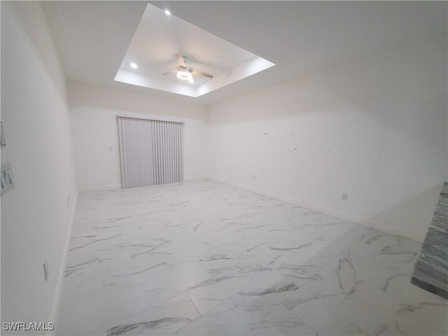 unfurnished room featuring a ceiling fan, a raised ceiling, baseboards, and marble finish floor