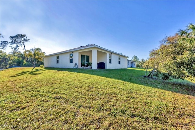 rear view of property featuring a lawn and stucco siding