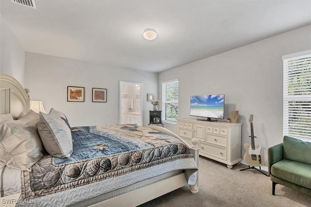 bedroom with visible vents, light carpet, and ensuite bathroom