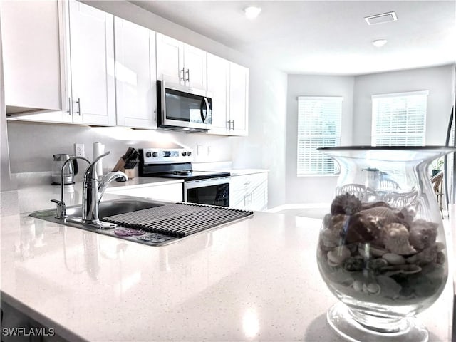 kitchen featuring light stone counters, visible vents, white cabinets, and stainless steel appliances