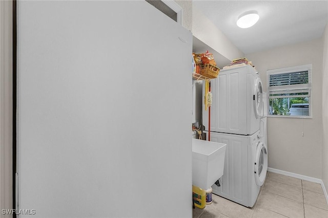 washroom featuring light tile patterned floors, baseboards, laundry area, a sink, and stacked washer and clothes dryer