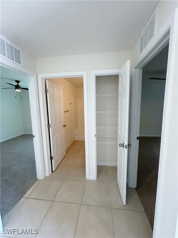 corridor with light tile patterned floors, visible vents, and light carpet