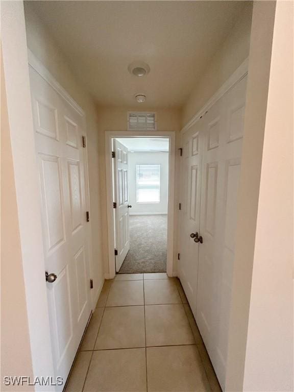 hallway featuring light tile patterned floors, visible vents, and light colored carpet