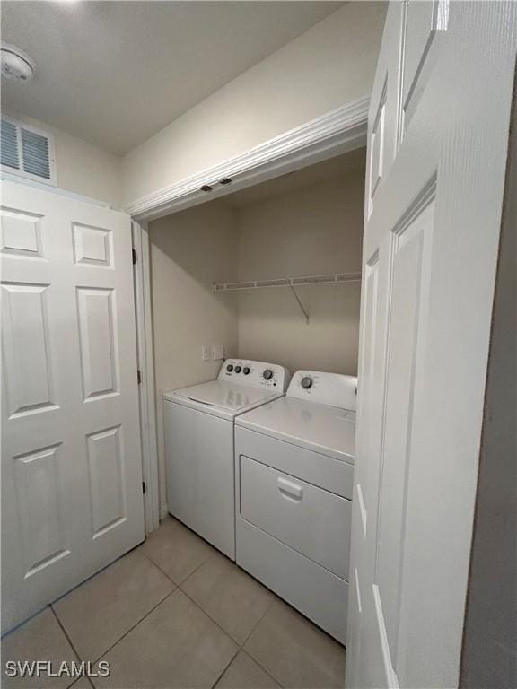 clothes washing area featuring laundry area, light tile patterned flooring, visible vents, and washer and clothes dryer