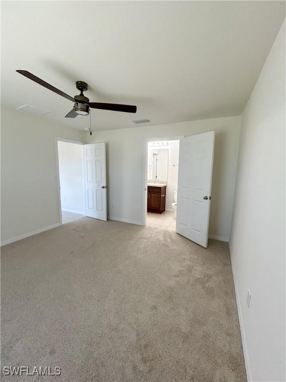 unfurnished bedroom featuring baseboards, light colored carpet, ensuite bath, and a ceiling fan