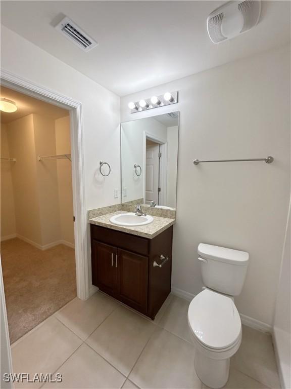 bathroom with tile patterned floors, visible vents, toilet, vanity, and a spacious closet