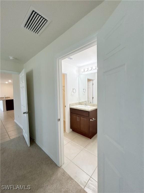 hallway featuring light tile patterned floors, visible vents, light colored carpet, and a sink