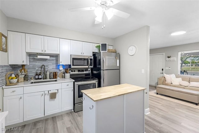 kitchen with a ceiling fan, a sink, appliances with stainless steel finishes, white cabinetry, and butcher block counters