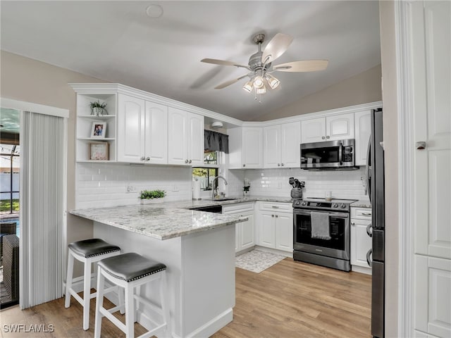 kitchen featuring a ceiling fan, a peninsula, vaulted ceiling, white cabinets, and appliances with stainless steel finishes