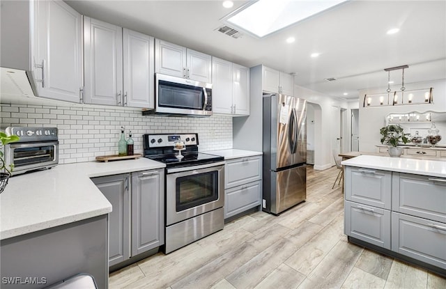 kitchen featuring visible vents, a skylight, gray cabinets, stainless steel appliances, and light wood-style floors