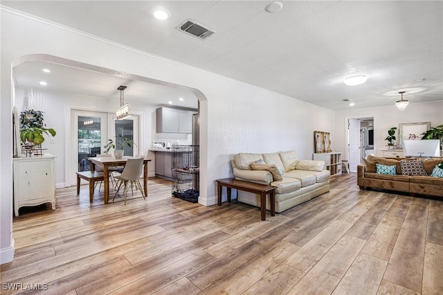 living area with visible vents, recessed lighting, arched walkways, light wood-style floors, and crown molding