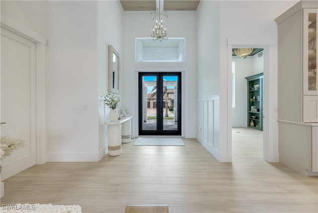 foyer with a notable chandelier, french doors, light wood-style floors, and a towering ceiling